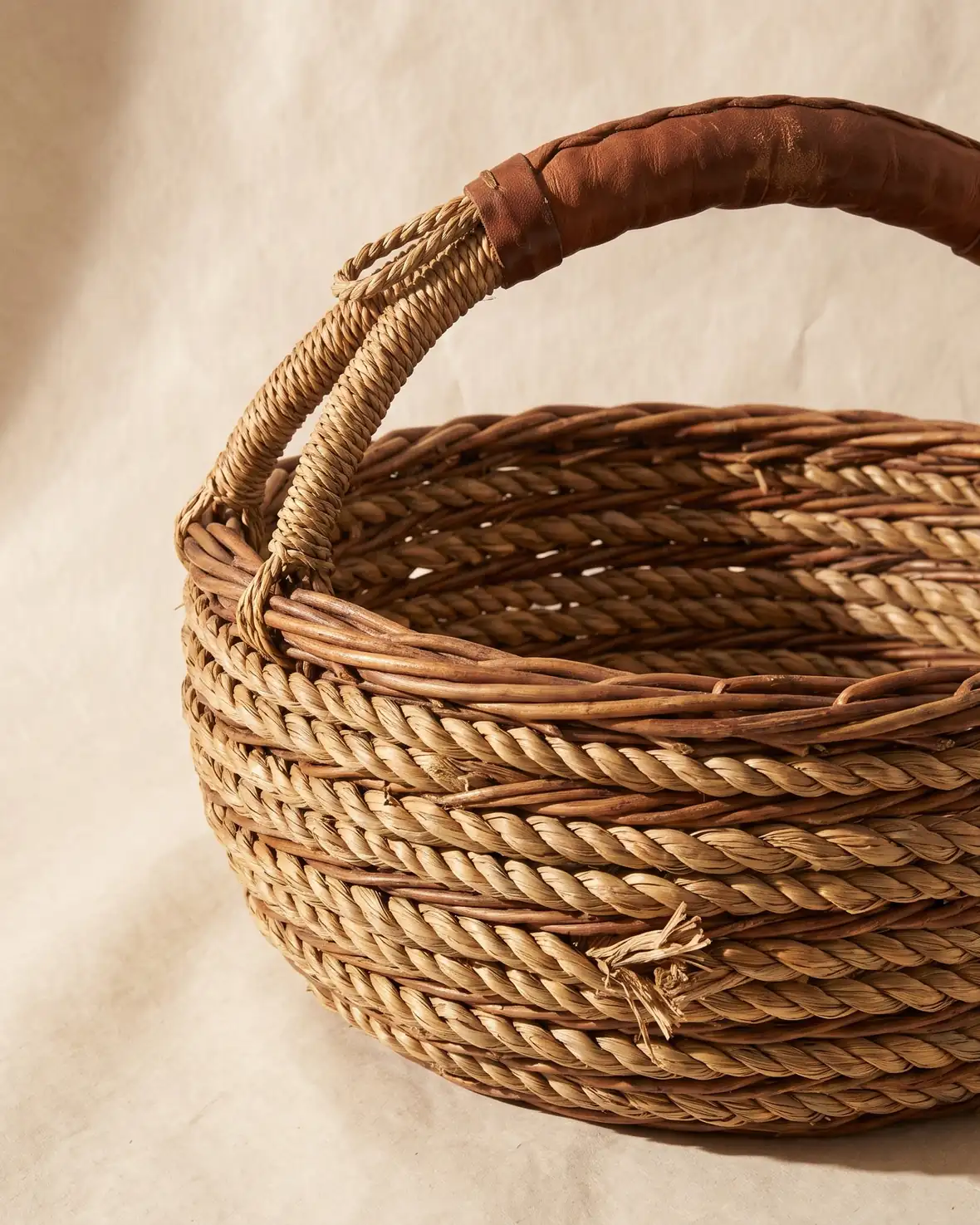 A large coiled willow gathering basket with a worn handle on a warm paper sweep.