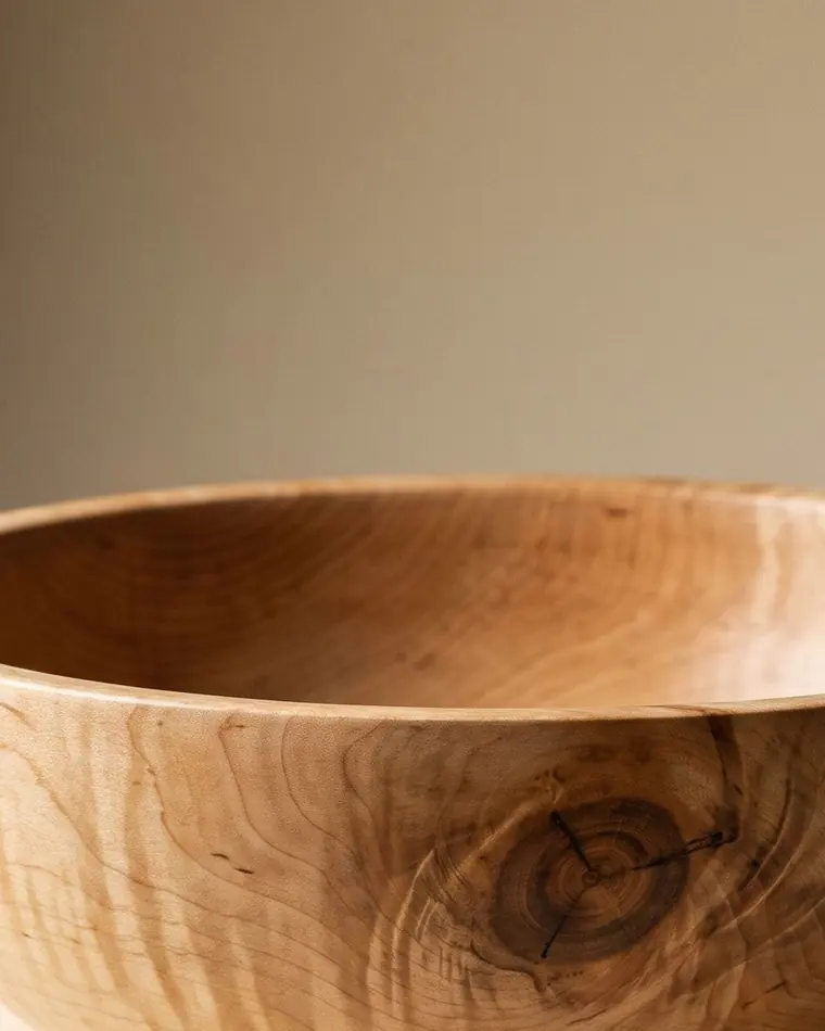 A close view of a small turned figured maple serving bowl on a warm paper sweep.