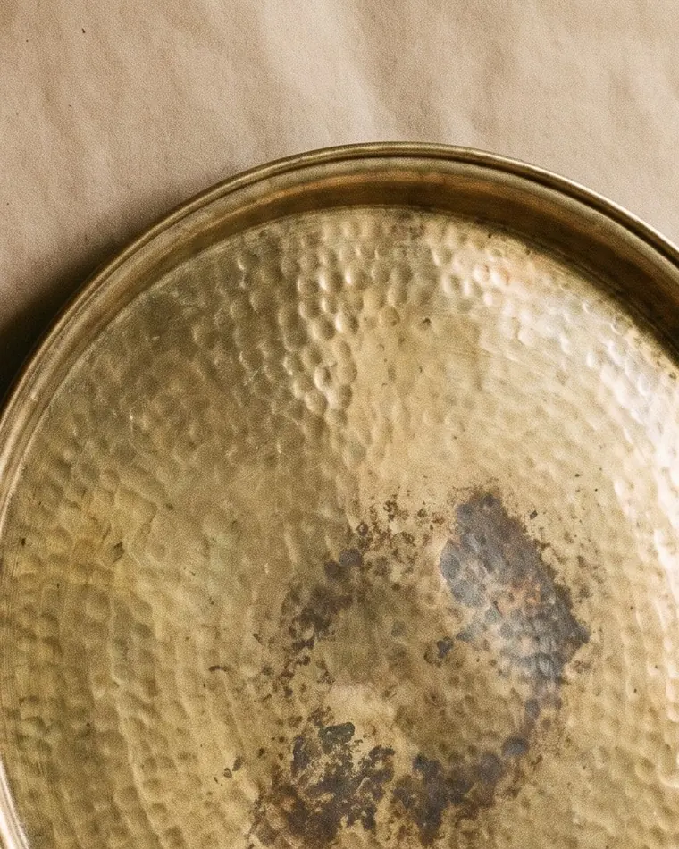 A close view of a small hammered brass dish with warm patina on a warm paper sweep.