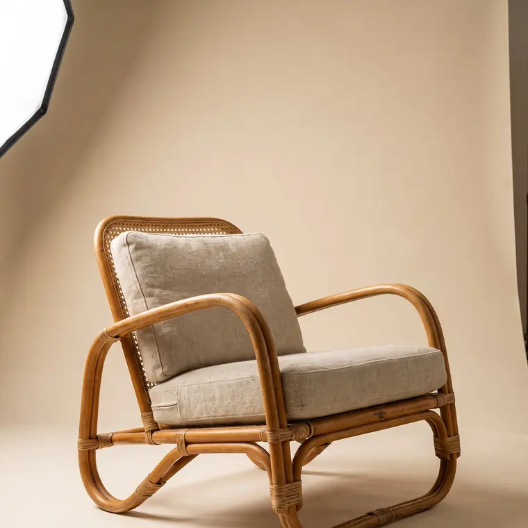 A bentwood rattan and cane lounge chair with a loose oatmeal linen cushion on a warm paper sweep — upper detail.