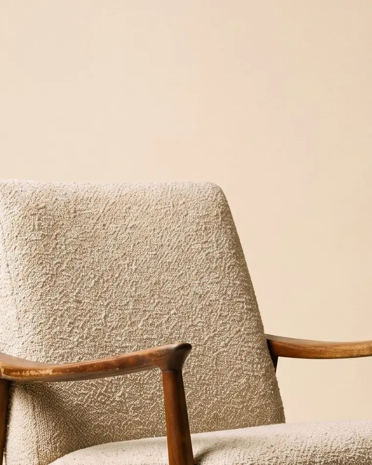 A close view of a walnut-framed mid-century armchair in oatmeal bouclé on a warm paper sweep.