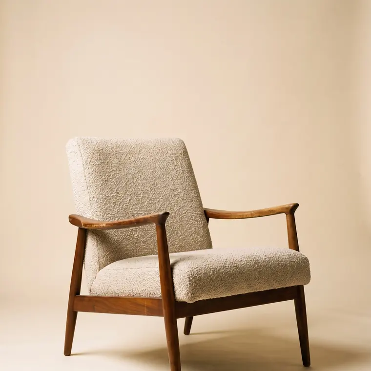 A mid-century lounge chair with an oiled walnut frame and oatmeal bouclé upholstery on a warm paper sweep — upper detail.