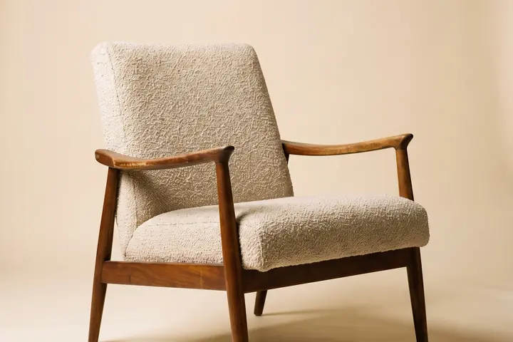 A walnut-framed mid-century lounge chair in oatmeal boucle on a warm paper sweep