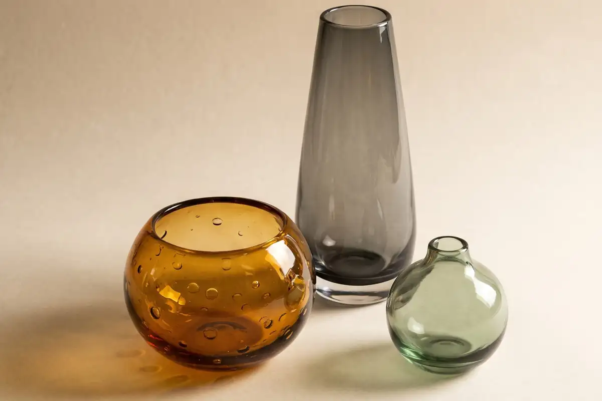 A close view of an amber hand-blown glass bubble bowl throwing warm caustic light onto a warm paper sweep — full width on the paper sweep.