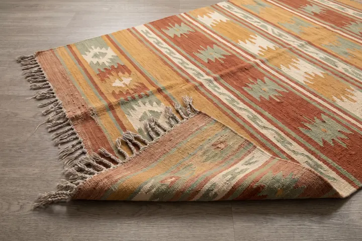 A flatwoven wool rug in ochre, rust and sage bands photographed from above
