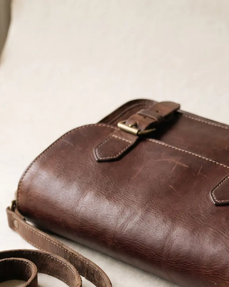 A close view of a chestnut hand-stitched leather document folio on warm paper.