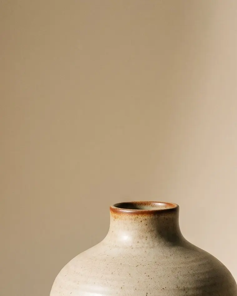 A tall thrown stoneware vase in iron slip over a bone body, close-up on a warm paper sweep.