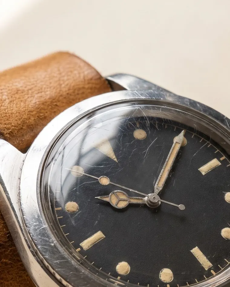 A close view of a vintage steel skin-diver watch with a browned tropical dial on warm paper.