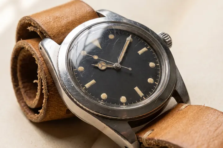 A vintage steel dive watch with a faded dial and a worn tan strap