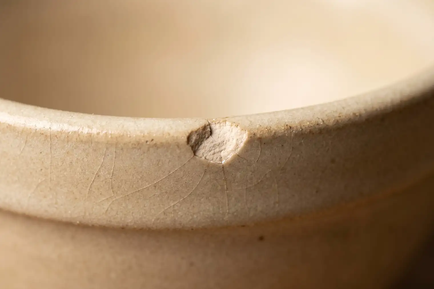 Macro photograph of a chipped stoneware rim showing the pale clay body beneath the glaze, with fine crazing nearby